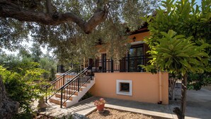 Una casa con una escalera que lleva a un balcón, rodeada de árboles y un muro de piedra.