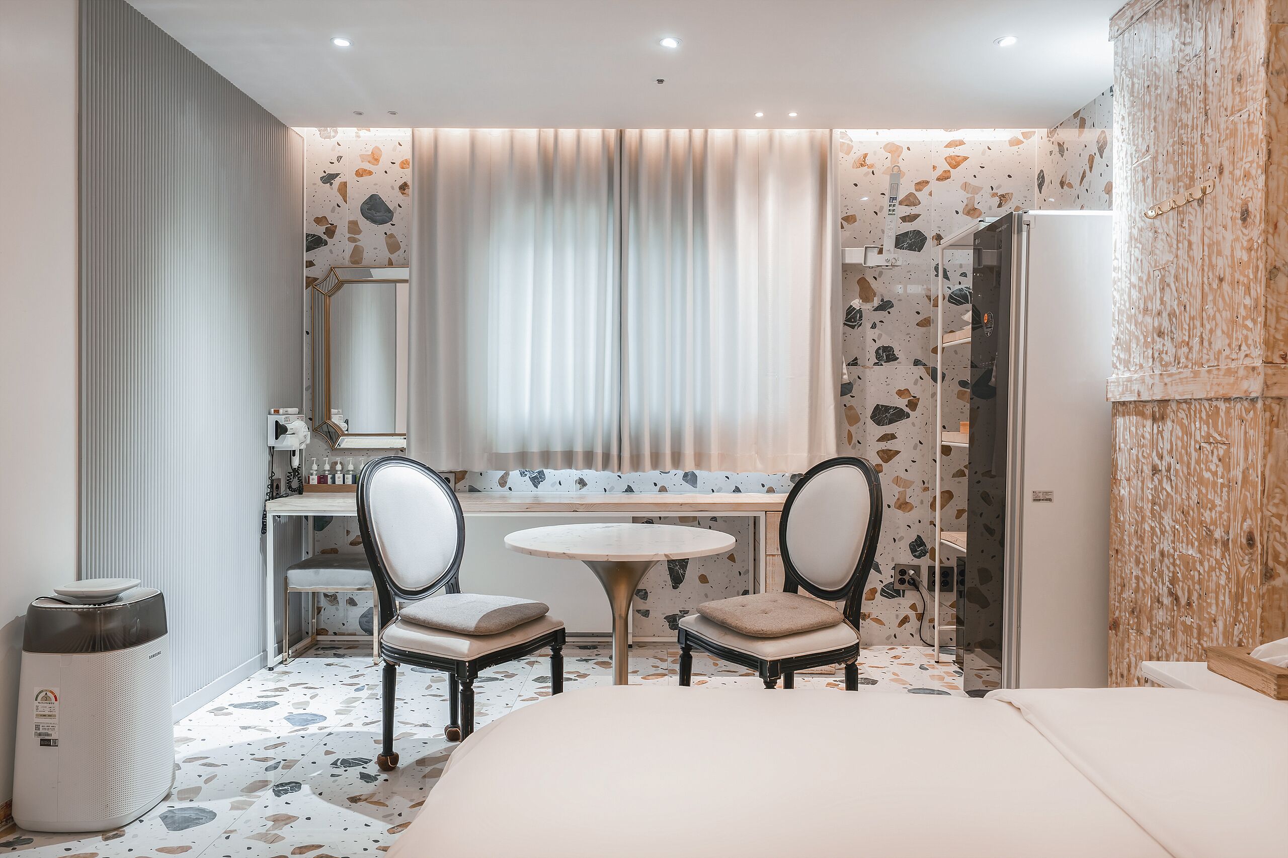 A modern hotel room with a bed, two chairs, a round table, a mirror, a sink, and a wardrobe.
