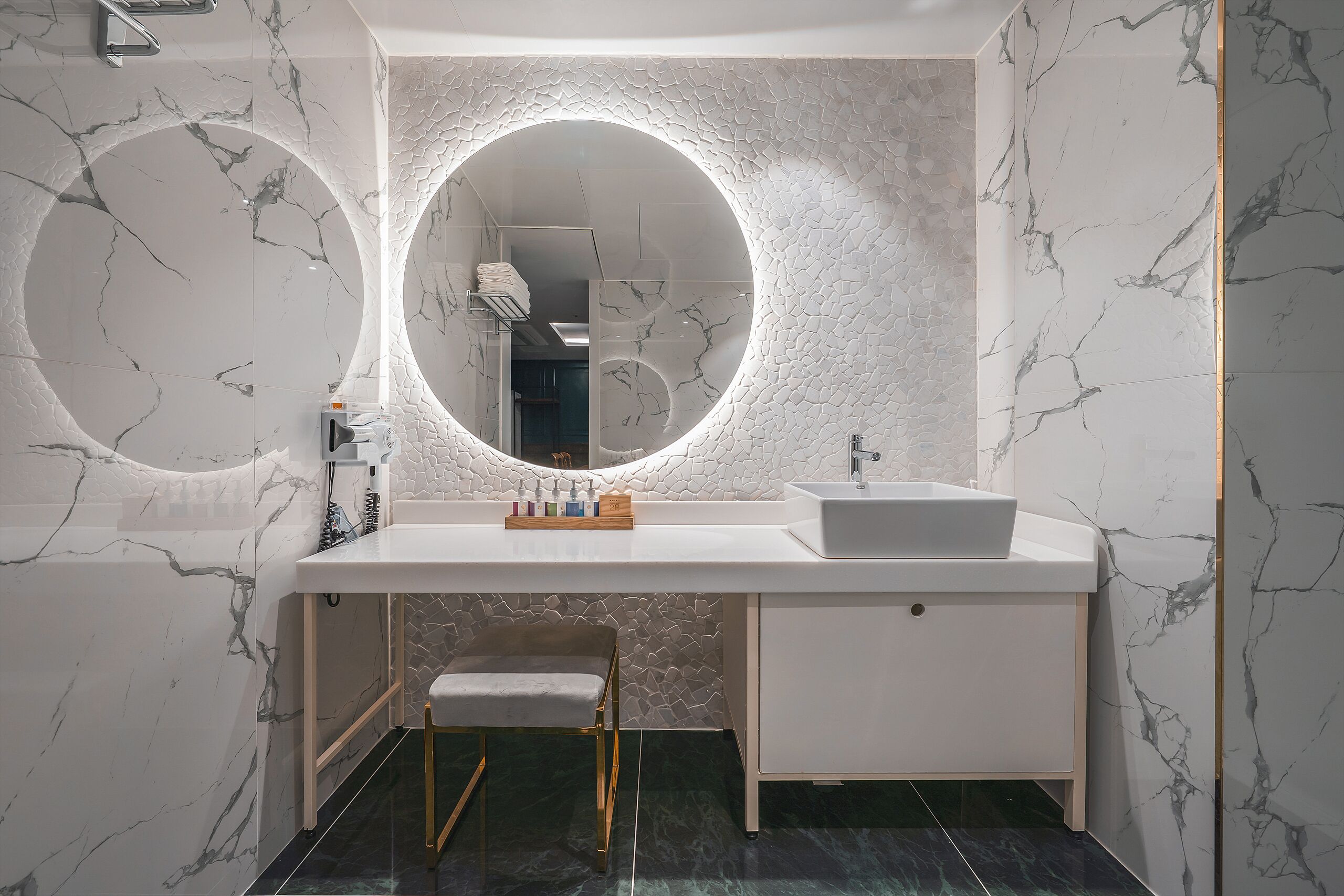 A modern bathroom with a marble vanity, a round mirror, and a small stool.
