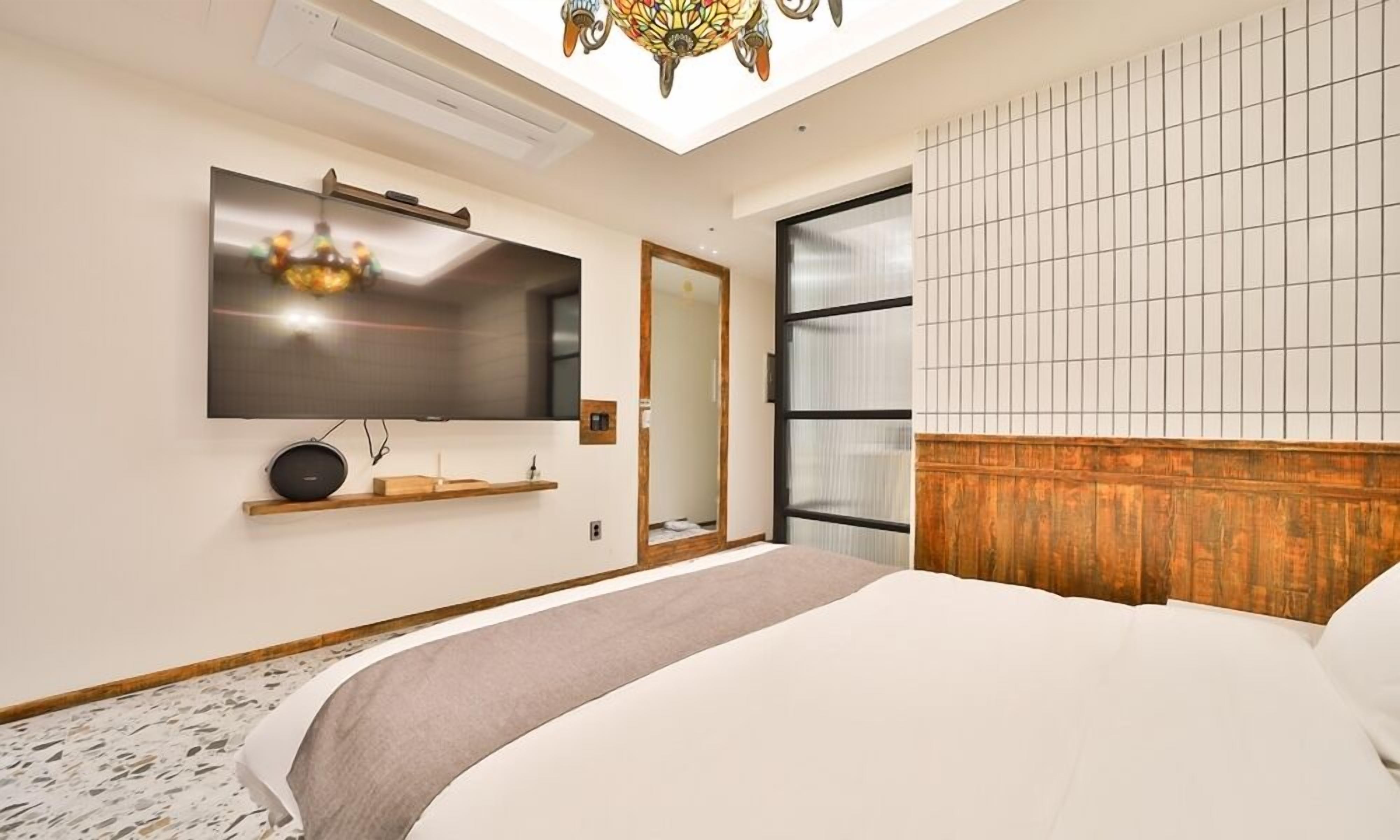 A modern bedroom with a large bed, a mounted TV, a wooden headboard, and a skylight.