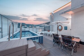 A rooftop pool area with a hot tub, lounge chairs, and a table with umbrellas.