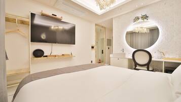 Une chambre d’hôtel moderne avec un grand lit, un téléviseur à écran plat fixé au mur, un miroir rond au-dessus du bureau et un lustre.