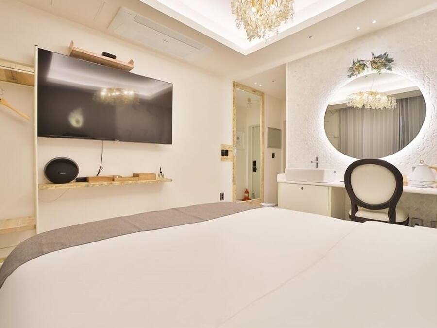 Une chambre d’hôtel moderne avec un grand lit, un téléviseur à écran plat fixé au mur, un miroir rond au-dessus du bureau et un lustre.