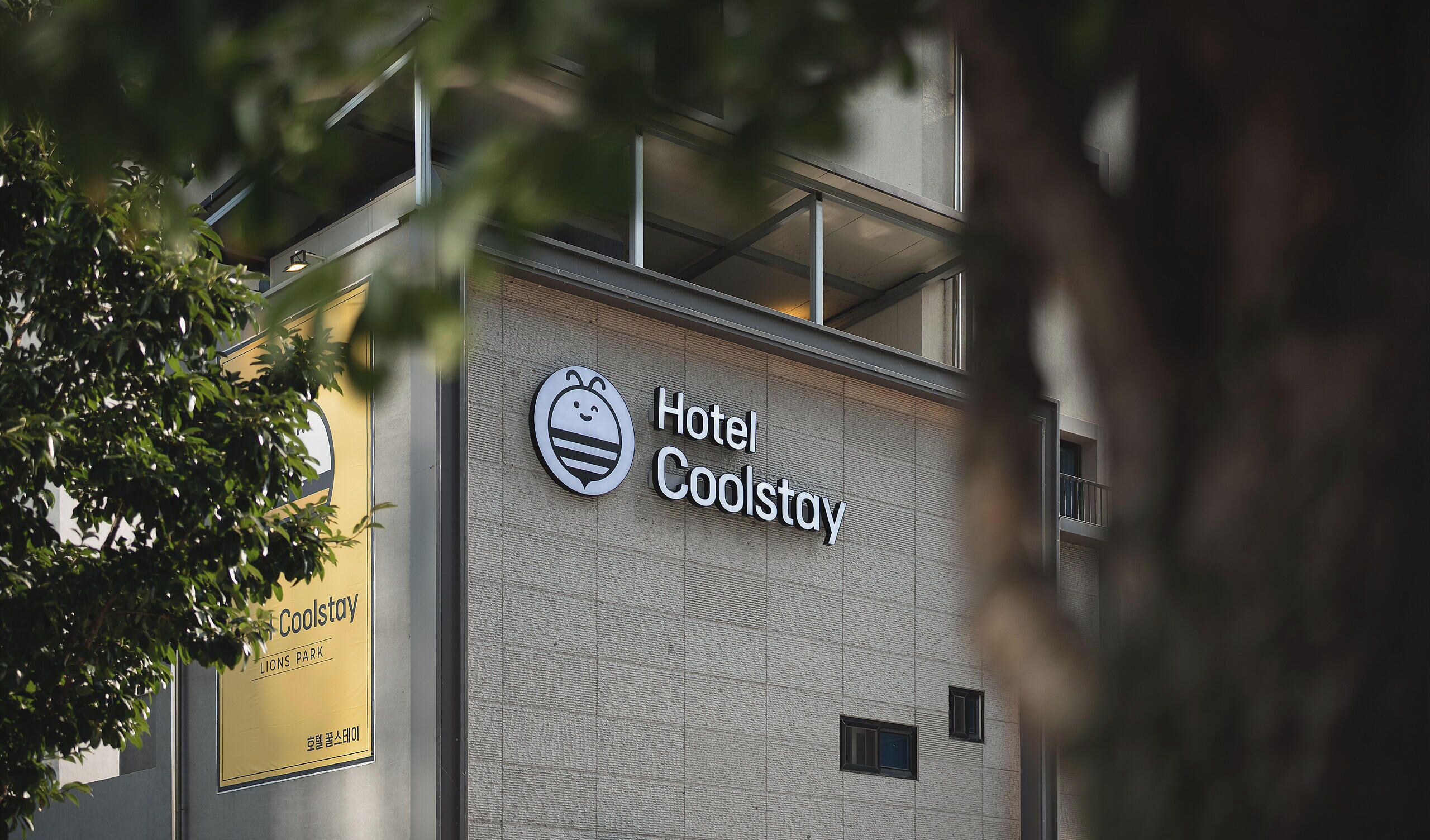 Une enseigne d’hôtel avec un logo représentant une abeille et le nom « Hotel Coolstay ».