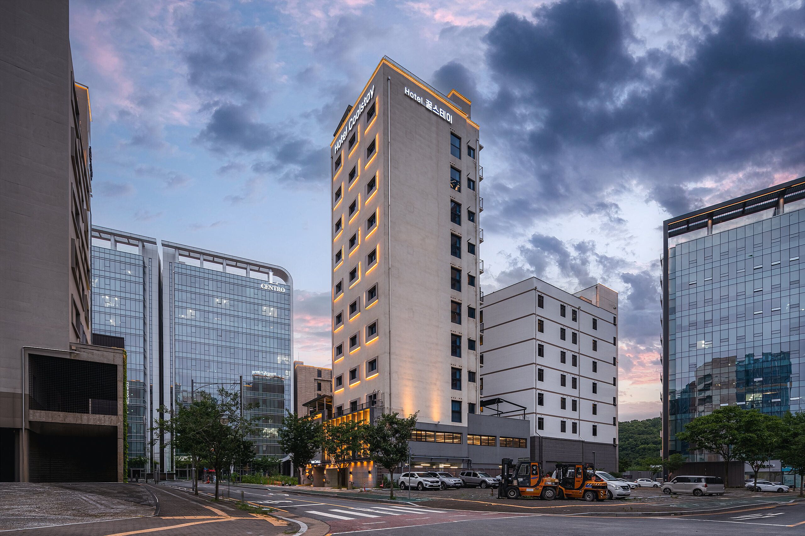 A multi-story hotel with a modern design, featuring a prominent entrance and a parking area in front.
