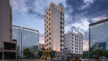 A multi-story hotel with a modern design, featuring a prominent entrance and a parking area in front.