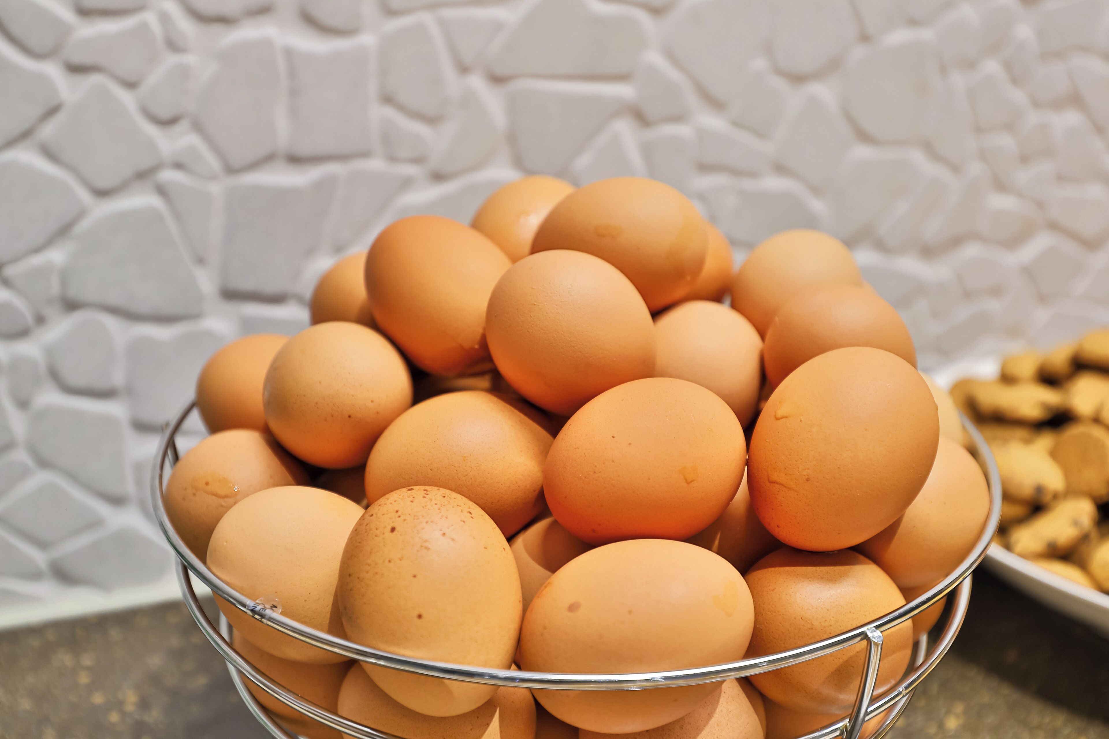 A metal bowl filled with brown eggs against a textured white wall.