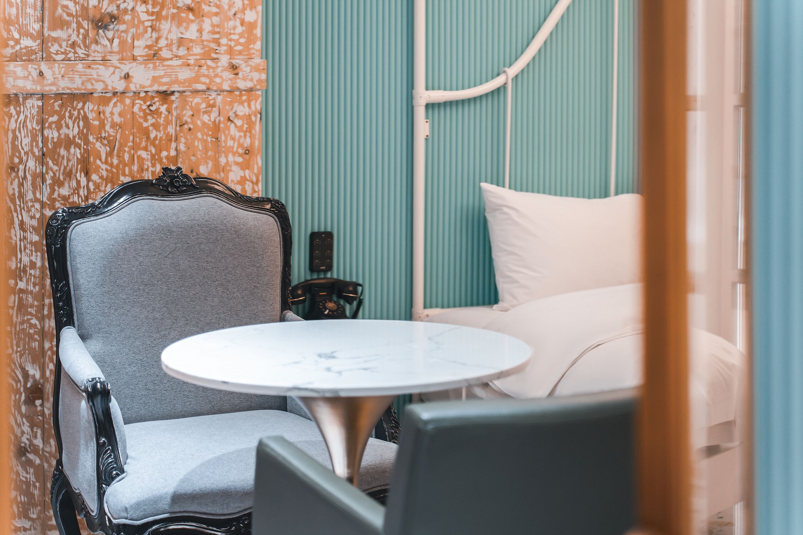 A room with a vintage-style chair, a small round table, and a bed with white bedding.