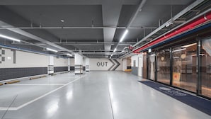 Un'ampia area di parcheggio sotterraneo moderna, con segnaletica direzionale chiara, un'uscita ben visibile e una facciata in vetro con un cartello che riporta 