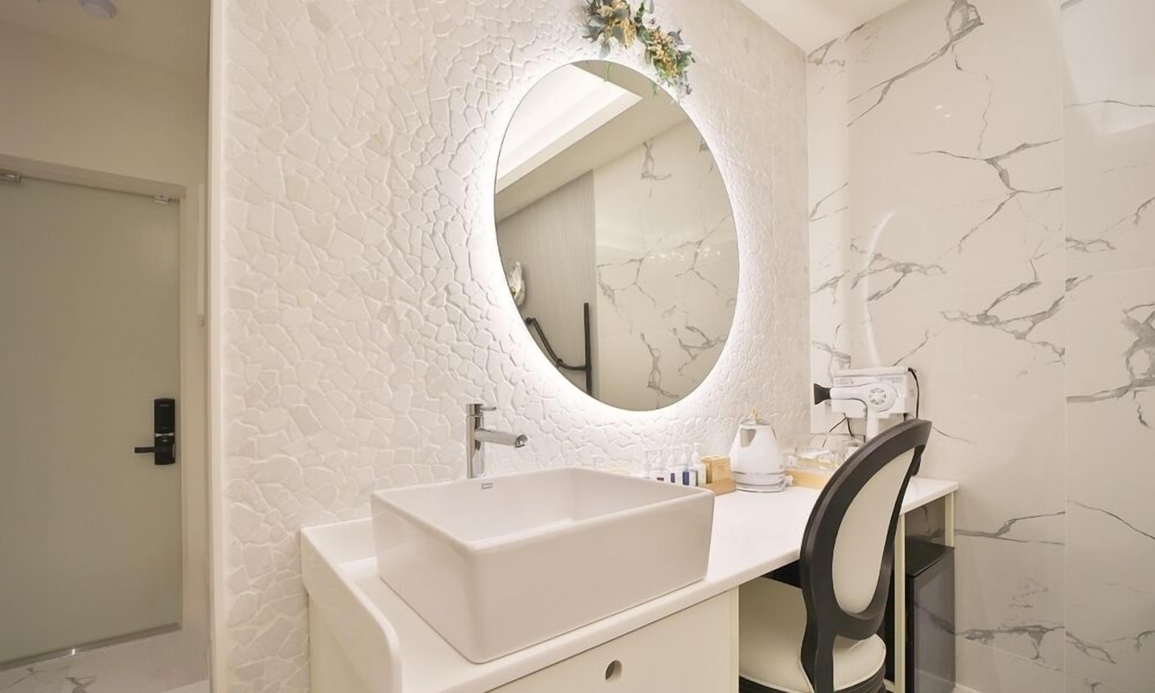 Un baño con un lavamanos blanco, un espejo redondo y una pared con diseño de mármol.