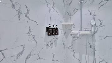A bathroom with a marble wall, a shower, and a soap dispenser mounted on the wall.