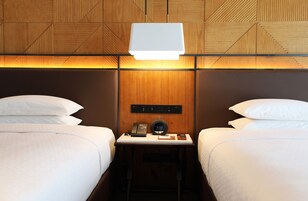 A hotel room with two beds, a bedside table with a phone, a clock, and a lamp.