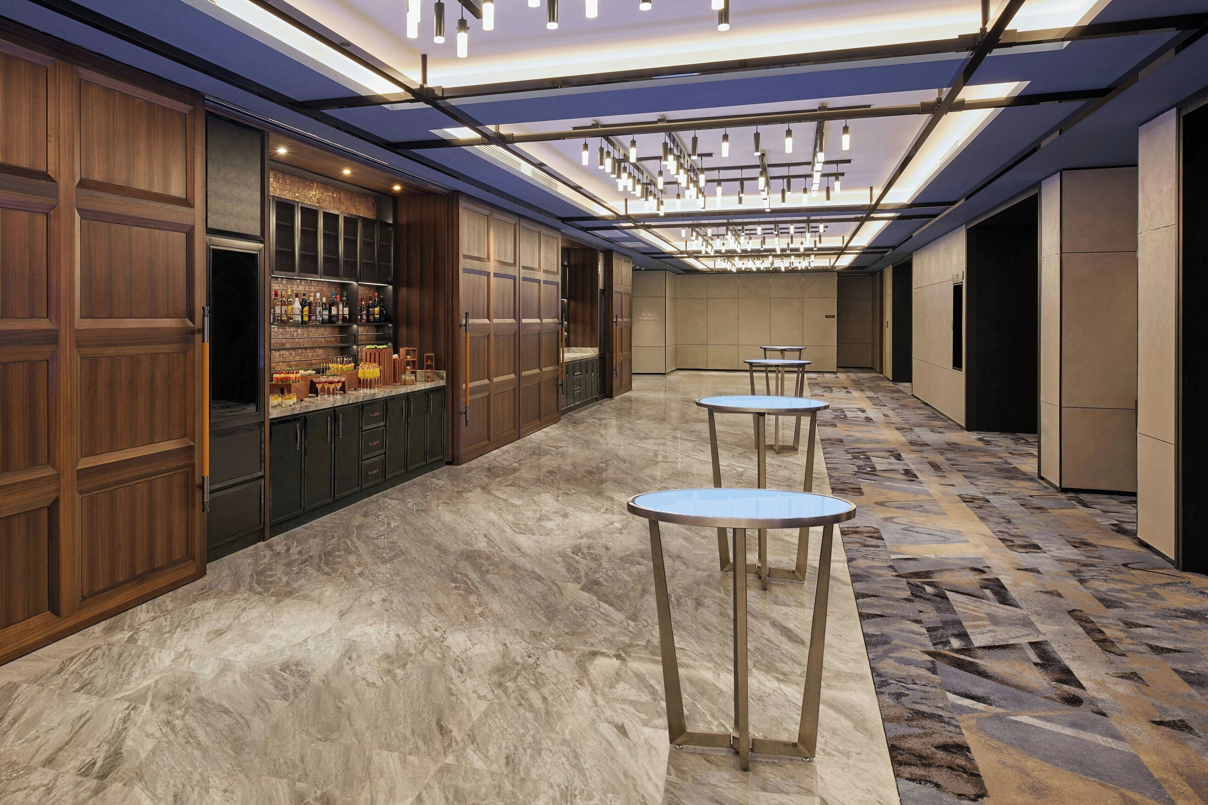 Eine moderne Hotelhalle mit Barbereich, Marmorboden und drei runden Tischen.