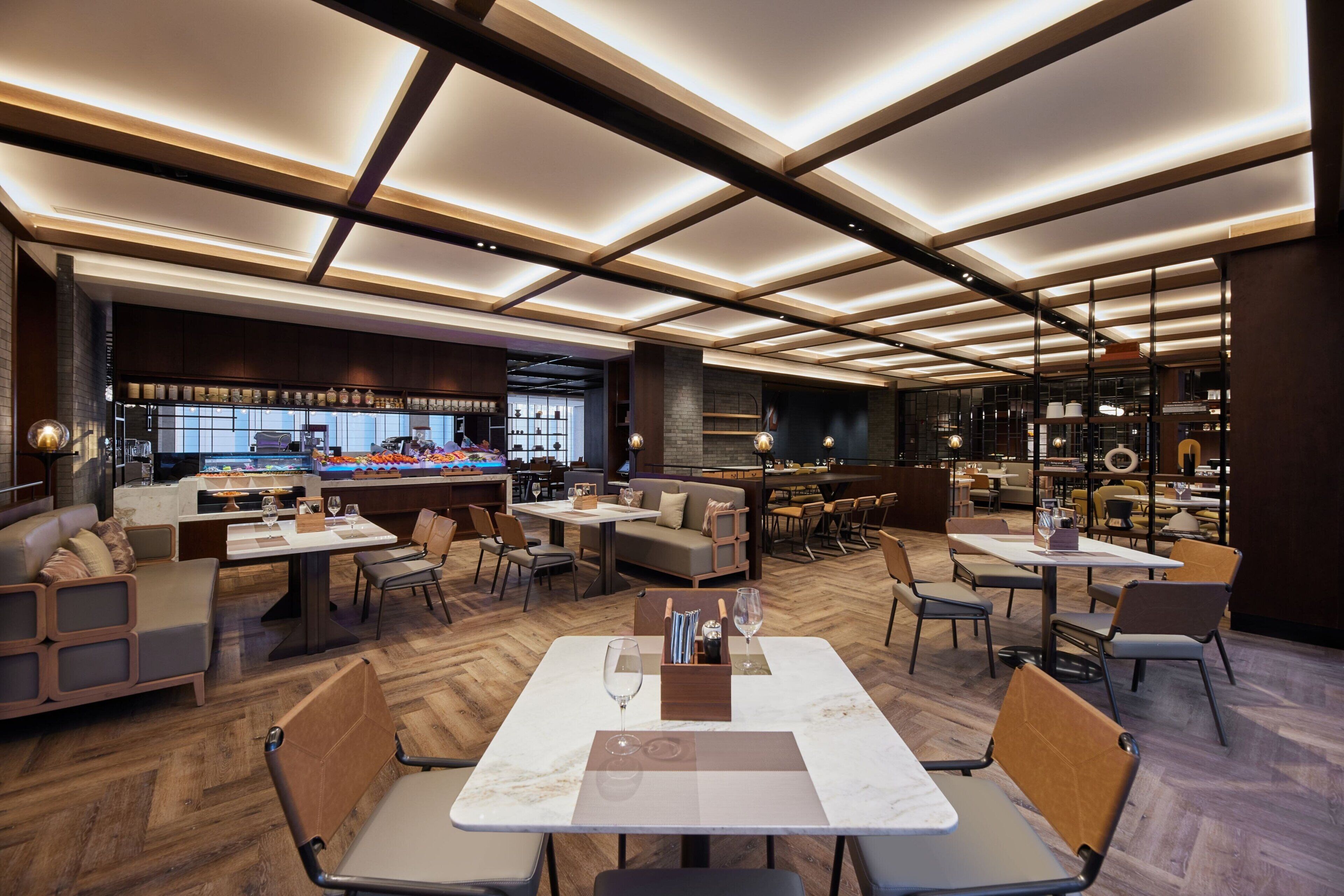 A modern restaurant with a central bar, multiple seating areas, and a wooden floor.