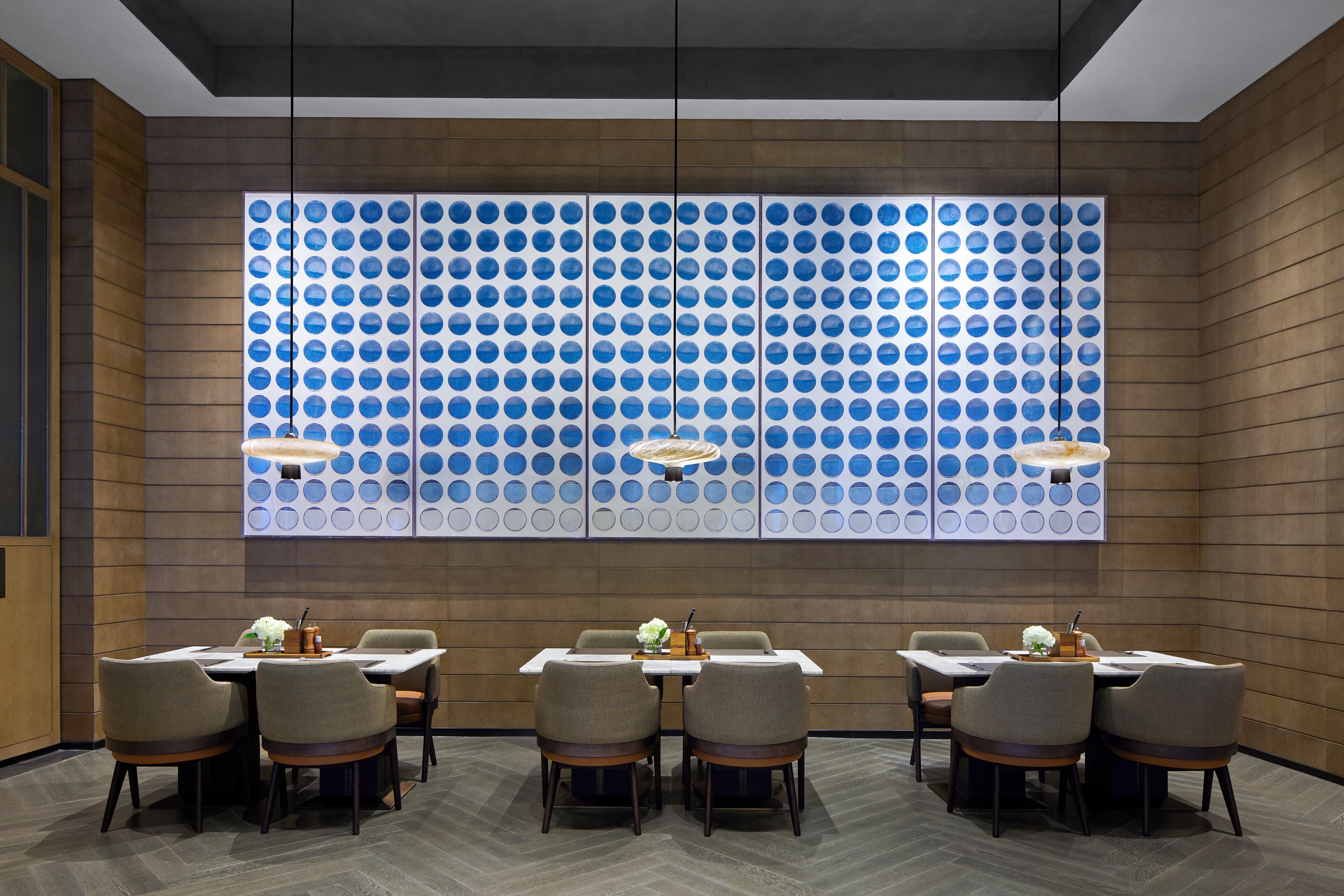 A modern dining area with a large wall of circular blue patterns, wooden paneling, and a herringbone floor.