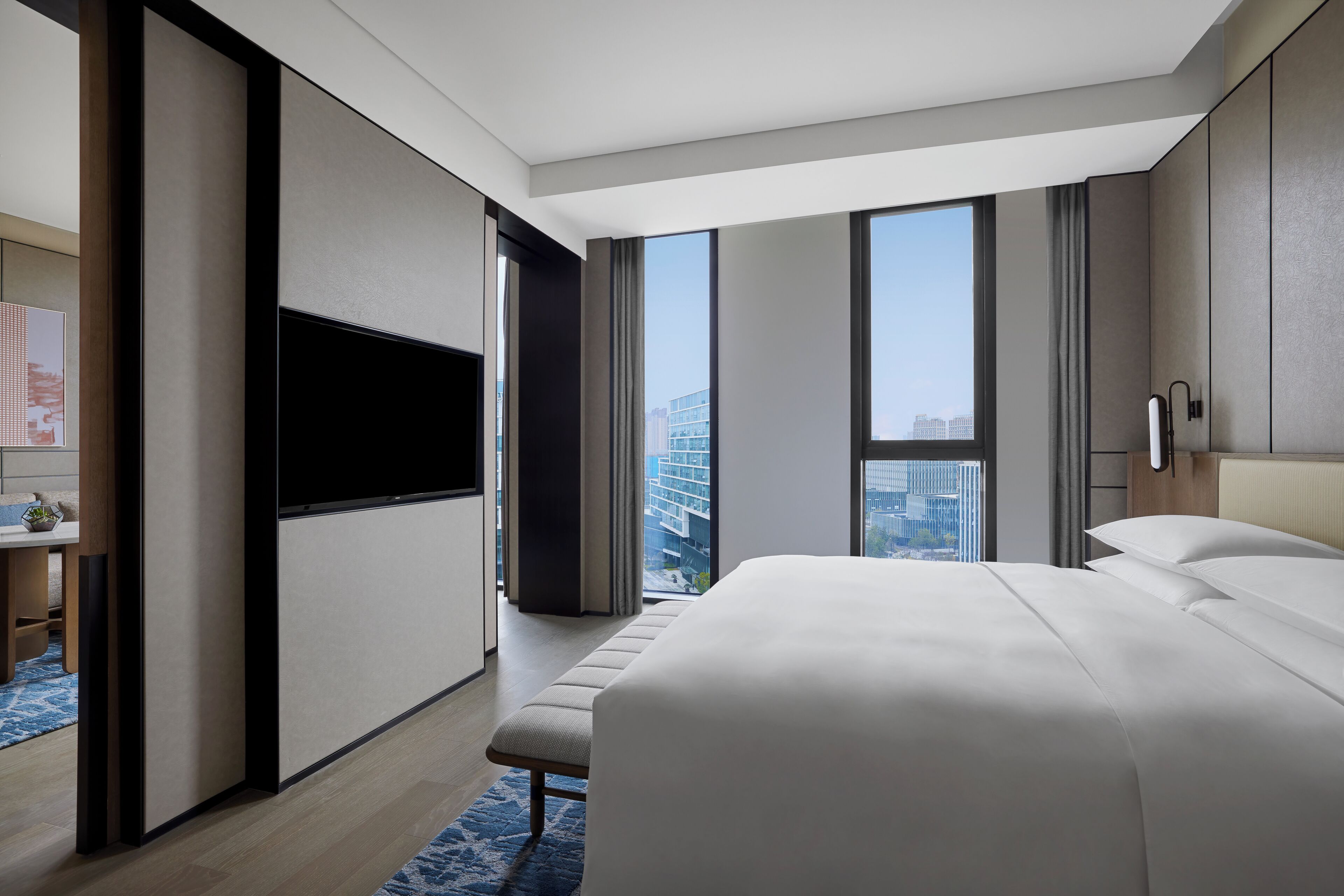 Una habitación de hotel moderna con una cama grande, un televisor de pantalla plana, un banco y vistas a la ciudad.