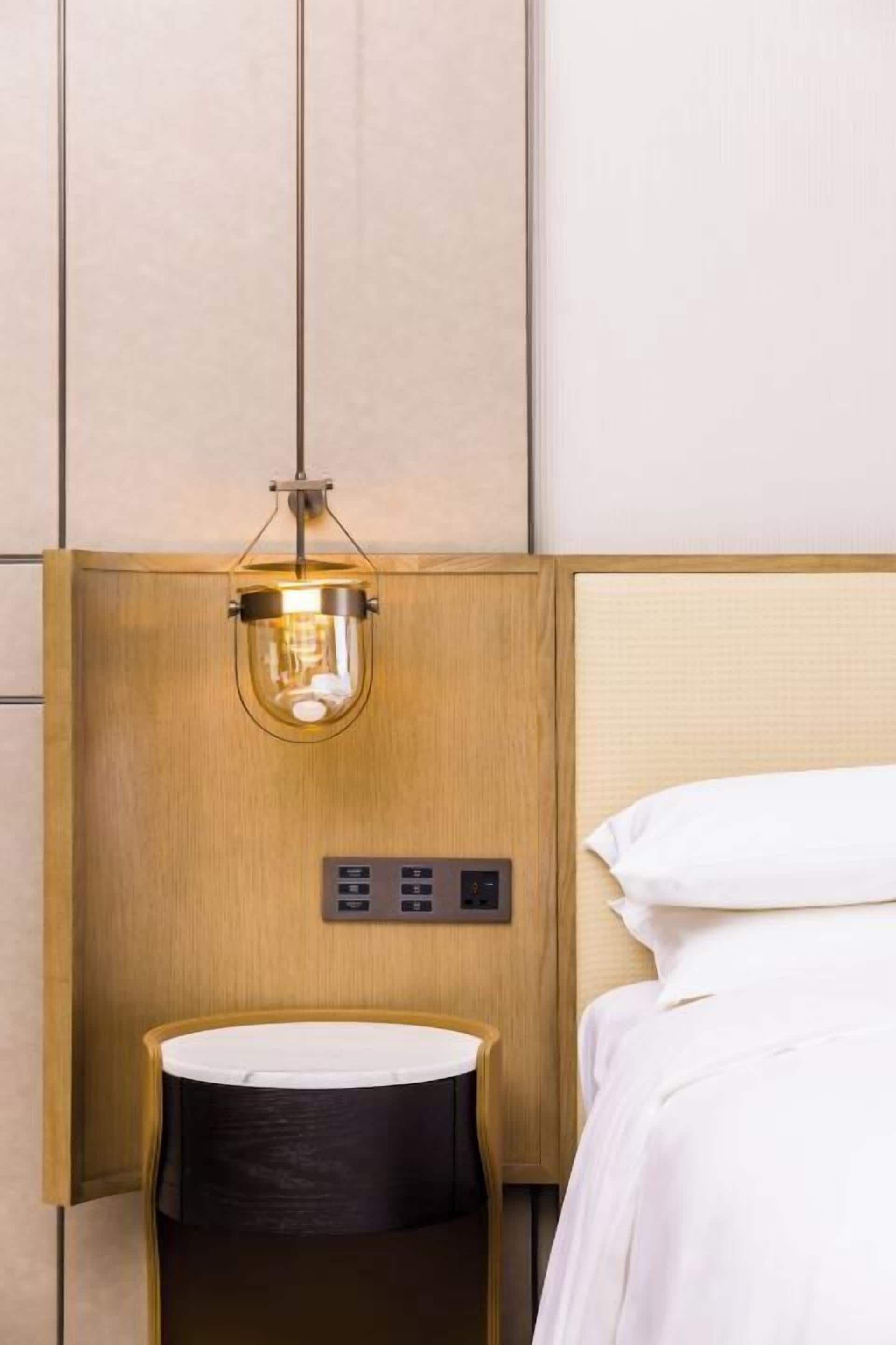 Ein Hotelzimmer mit einem Holzkopfteil, einem Nachttisch mit weißer Tischplatte und einer hängenden Leuchte.