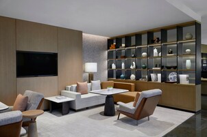 Un moderno vestíbulo de hotel con zonas de estar, televisión y una pared decorativa con estanterías.
