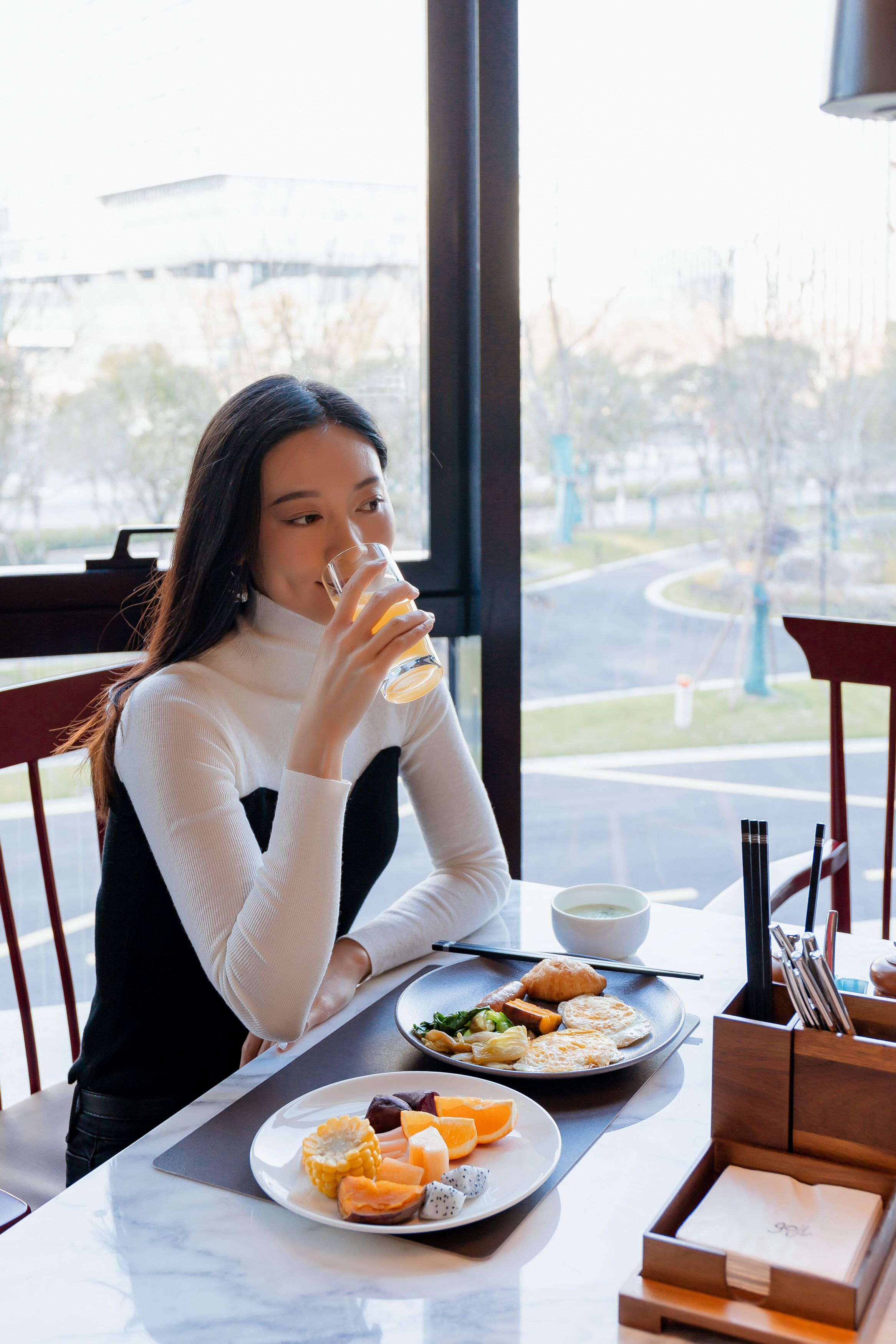 Una persona sentada a una mesa con comida, una ventana que da a una carretera y una silla.