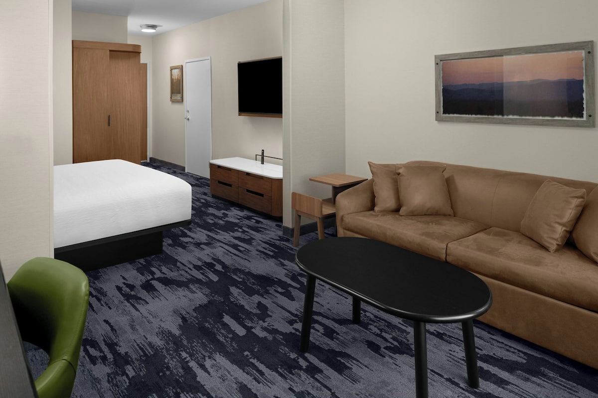 Ein Hotelzimmer mit Bett, Sofa, kleinem Tisch, Fernseher und einem Bild an der Wand.