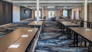 Une salle de conférence dotée de longues tables et de chaises, d’un sol recouvert de moquette et de grandes fenêtres.