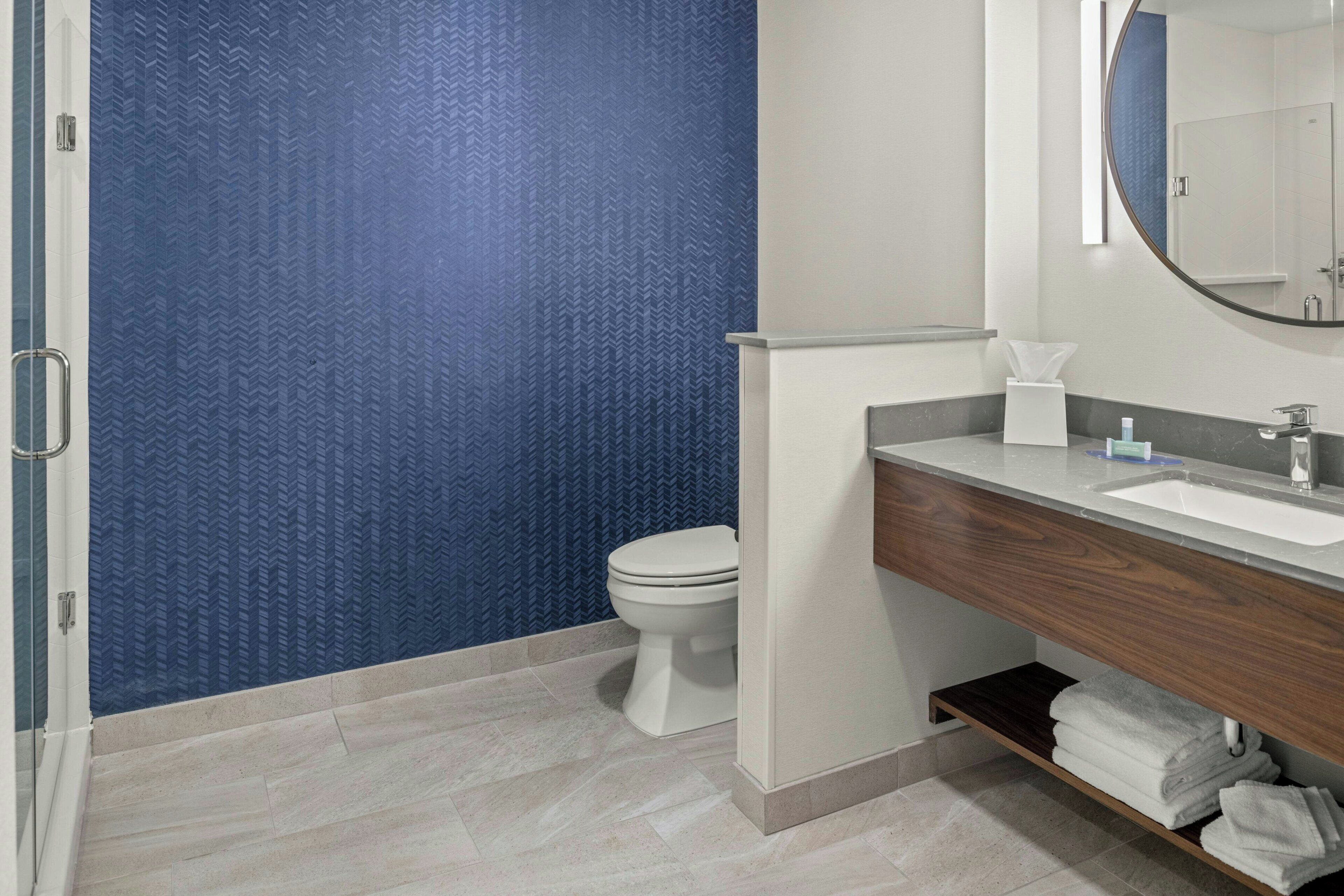 A bathroom with a blue textured wall, a white toilet, a wooden vanity with a sink, and a mirror.
