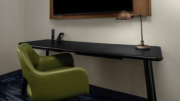A room with a black desk, a green chair, a lamp, and a television mounted on the wall.