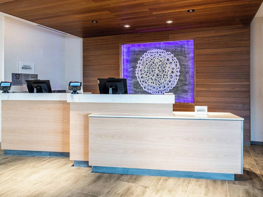 Un mostrador de recepción de hotel con diseño moderno, que incluye una zona de madera y una gran pieza decorativa en la pared.