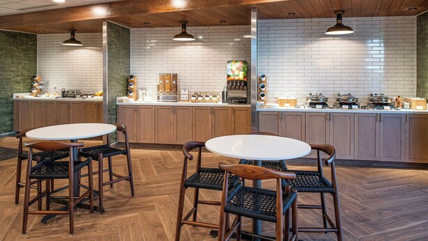 Un espace cuisine moderne avec des meubles en bois, un dosseret de carrelage blanc et un îlot central doté d’une machine à café.