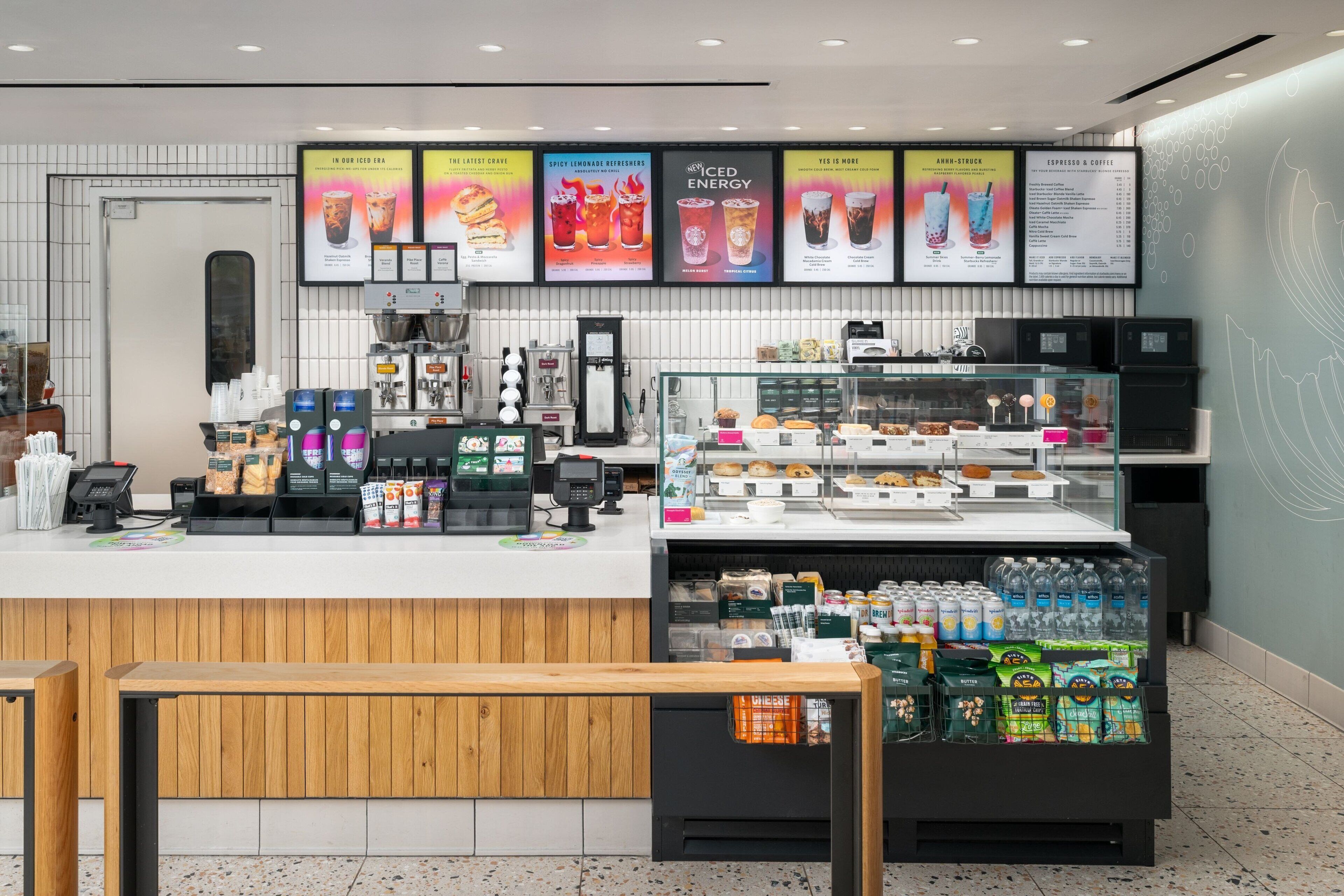 L'intérieur d'un café moderne présente un comptoir, des machines à café, un présentoir réfrigéré et un panneau affichant le menu, le tout placé au-dessus du comptoir.