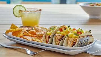A plate of tacos with a side of chips and a drink on a wooden table.