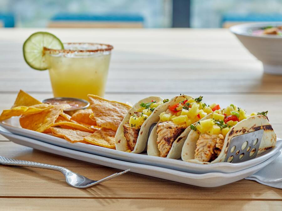 A plate of tacos with a side of chips and a drink on a wooden table.