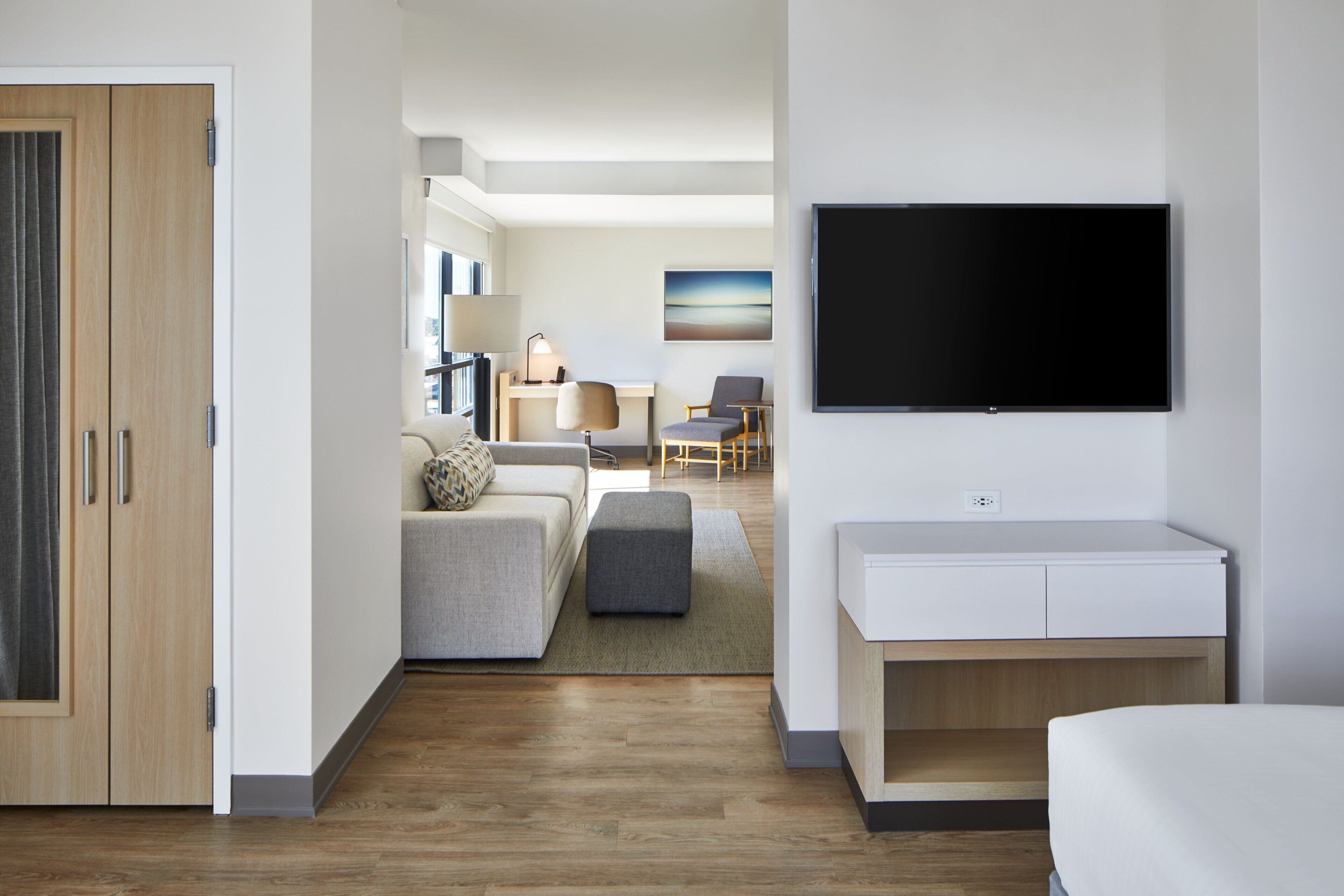 A modern hotel room with a wooden wardrobe, a sofa, a small table, a TV, and a bed.