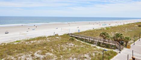 A beach with a wooden boardwalk, a sandy beach, and a few people.