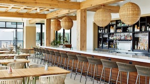 A bar area with wooden beams, wicker hanging lights, and a bar stocked with bottles.