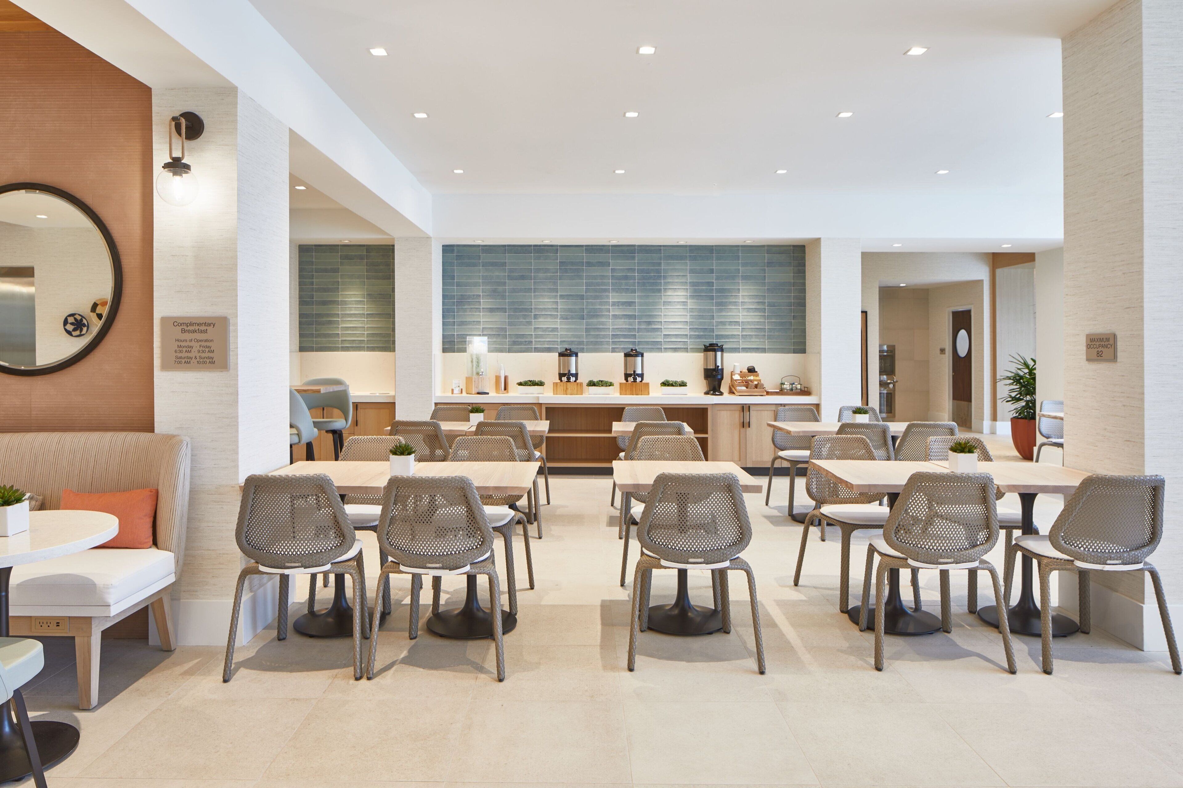 A modern dining area with round tables and wicker chairs, a large mirror, and a wall-mounted clock.