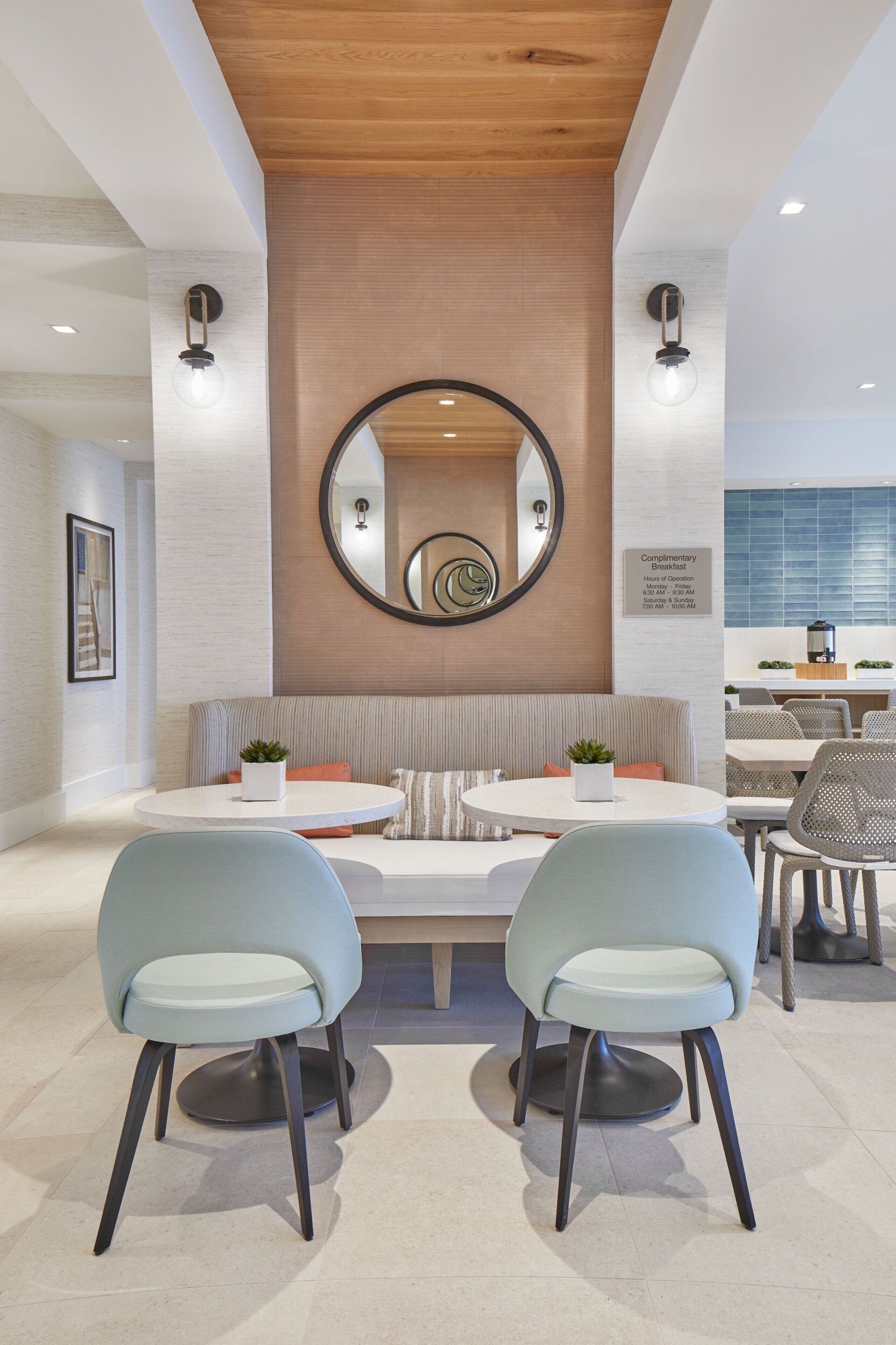 Un espace repas moderne avec une table ronde, deux chaises bleu clair, un plafond en bois et un miroir fixé au mur.
