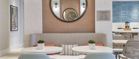A modern dining area with a round table, two light blue chairs, a wooden ceiling, and a wall-mounted mirror.