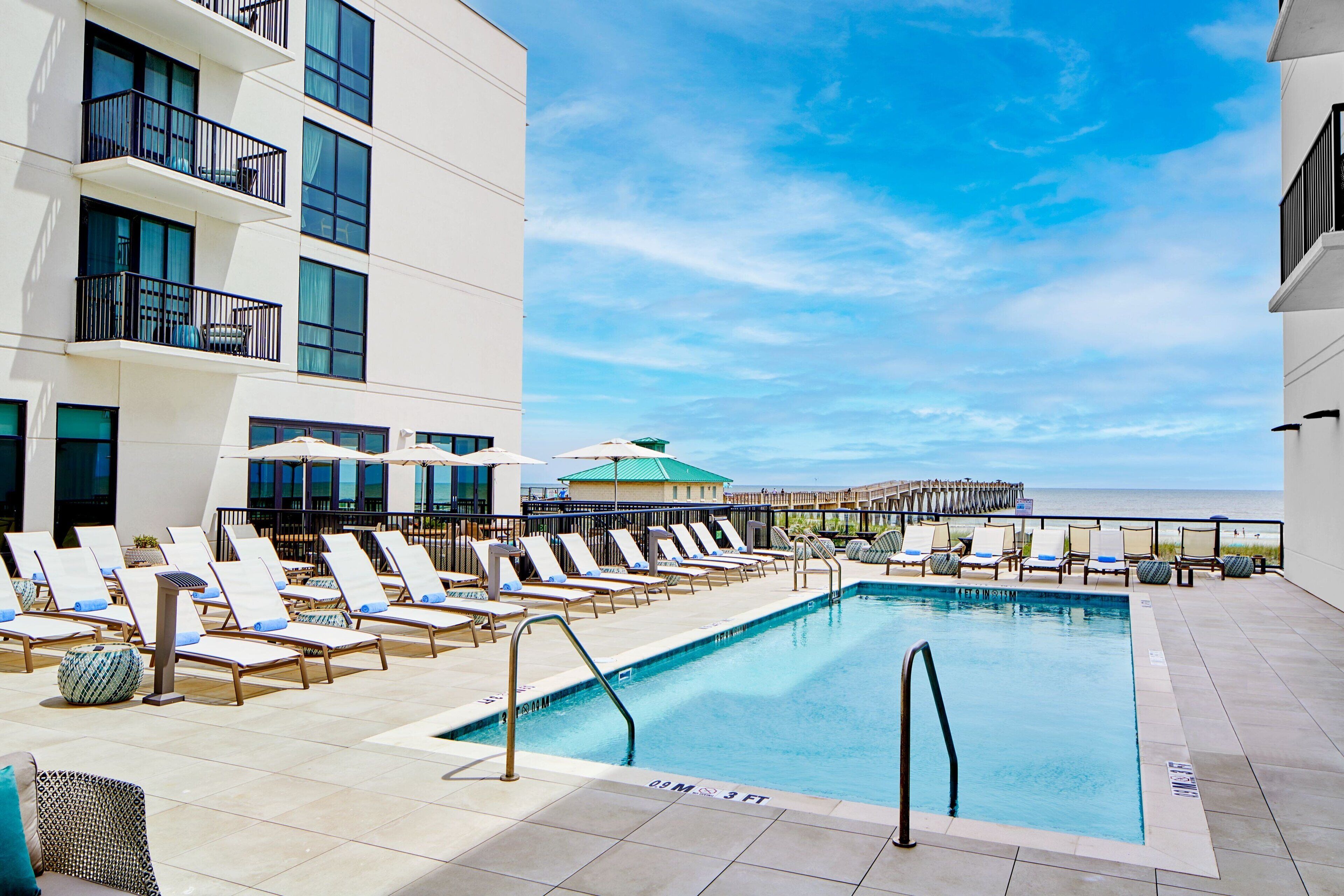 A poolside area with lounge chairs and a view of the ocean.