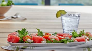 A plate of watermelon salad with feta cheese and greens, accompanied by a glass of water and a lime wedge.