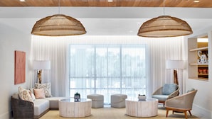 A modern living room with a sectional sofa, two round coffee tables, wicker chairs, and large windows with sheer curtains.