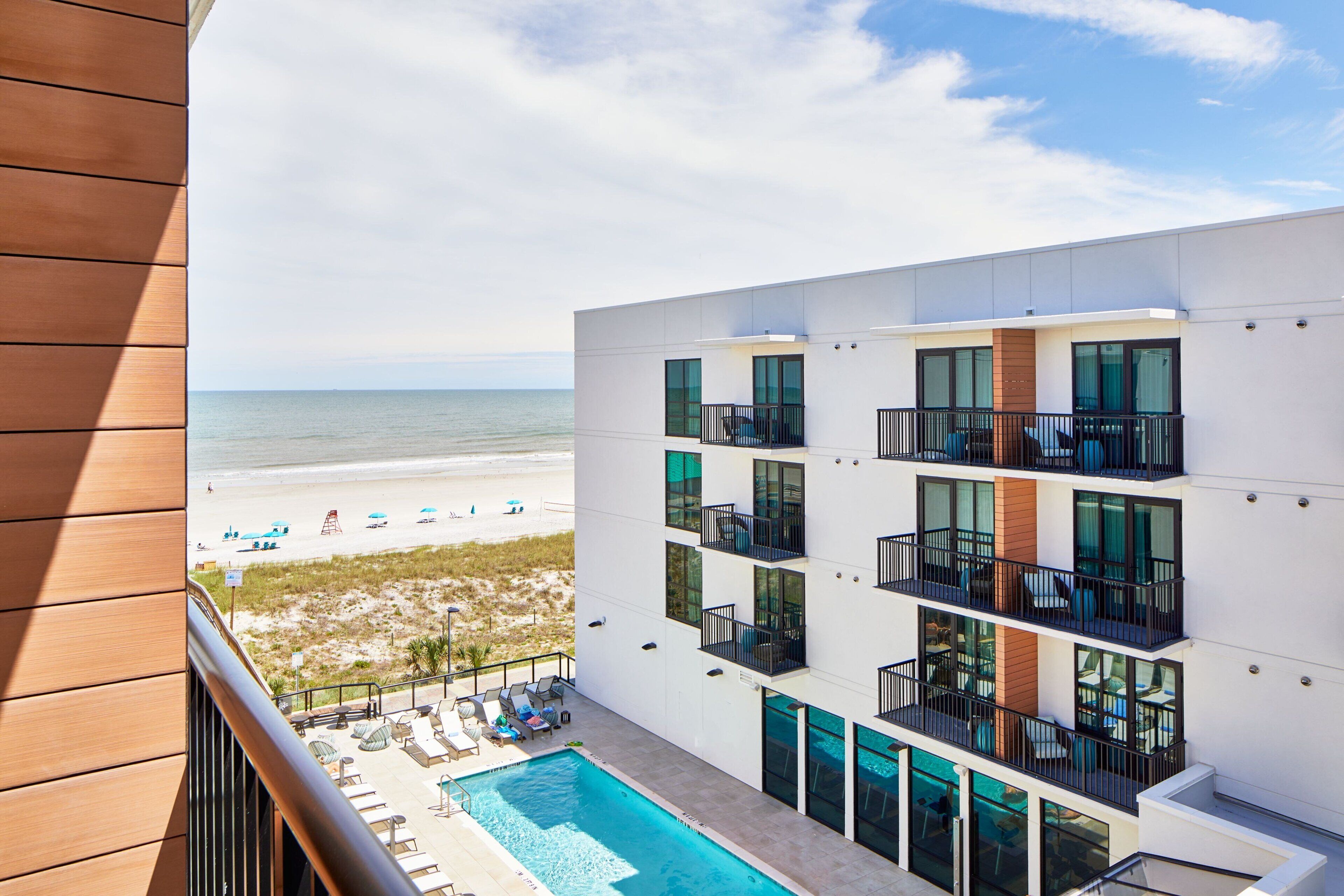 A modern hotel with a pool, balconies, and a beach view.