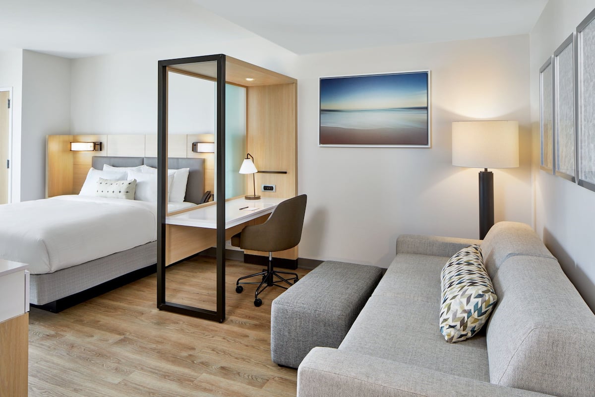 Ein Hotelzimmer mit zwei Betten, einem Schreibtisch, einem Sessel und einem Sofa, sowie einem großen Fenster mit Blick.