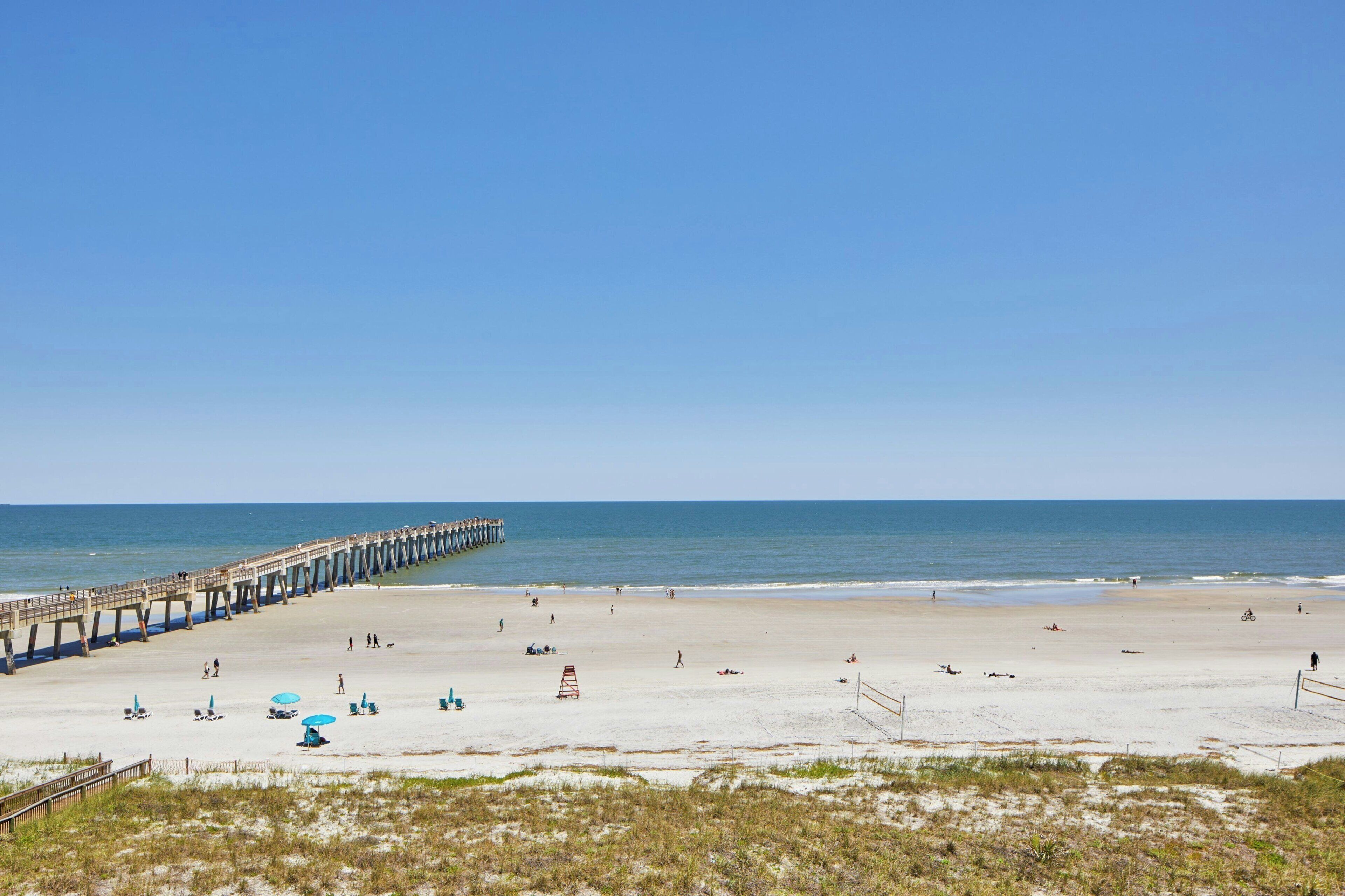 A beach with a pier extending into the water, sandy beach, and a few umbrellas.