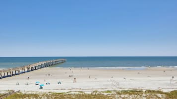 A beach with a pier extending into the water, sandy beach, and a few umbrellas.