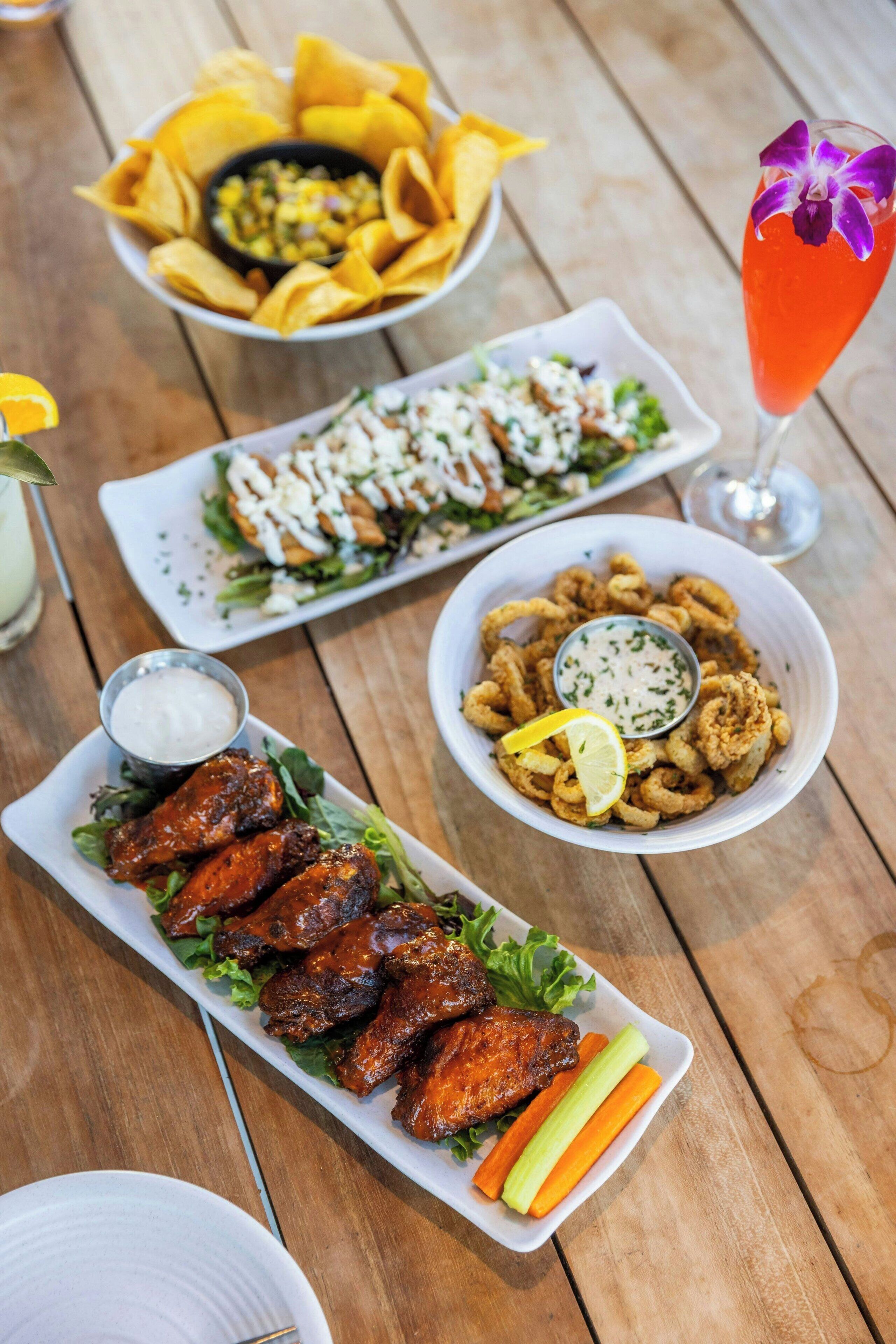 A table with various dishes including wings, salad, chips, and a cocktail.