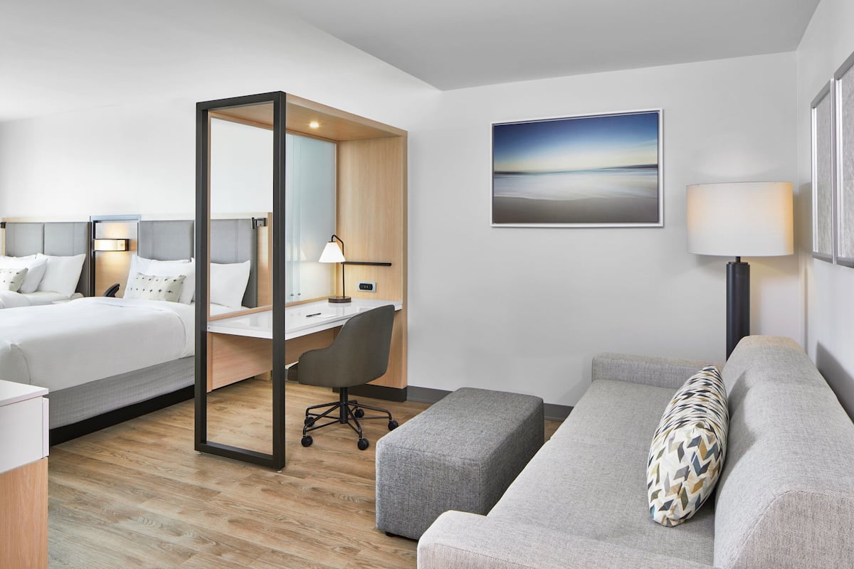 Ein Hotelzimmer mit zwei Betten, einem Schreibtisch, einem Stuhl, einer Couch und einem großen Spiegel.