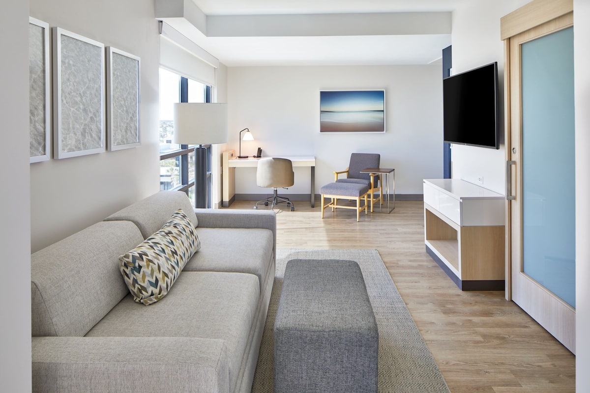 Ein modernes Wohnzimmer mit einer Couch, einem Schreibtisch, einem Stuhl, einem Fernseher und Kunstwerken an der Wand.