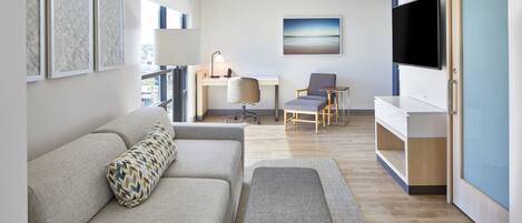 Una sala de estar moderna con un sofá, un escritorio, una silla, un televisor y obras de arte en la pared.