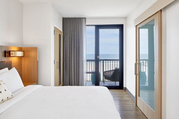 Habitación de hotel con una cama grande, vista al mar a través de un ventanal corredero y un balcón con una silla.